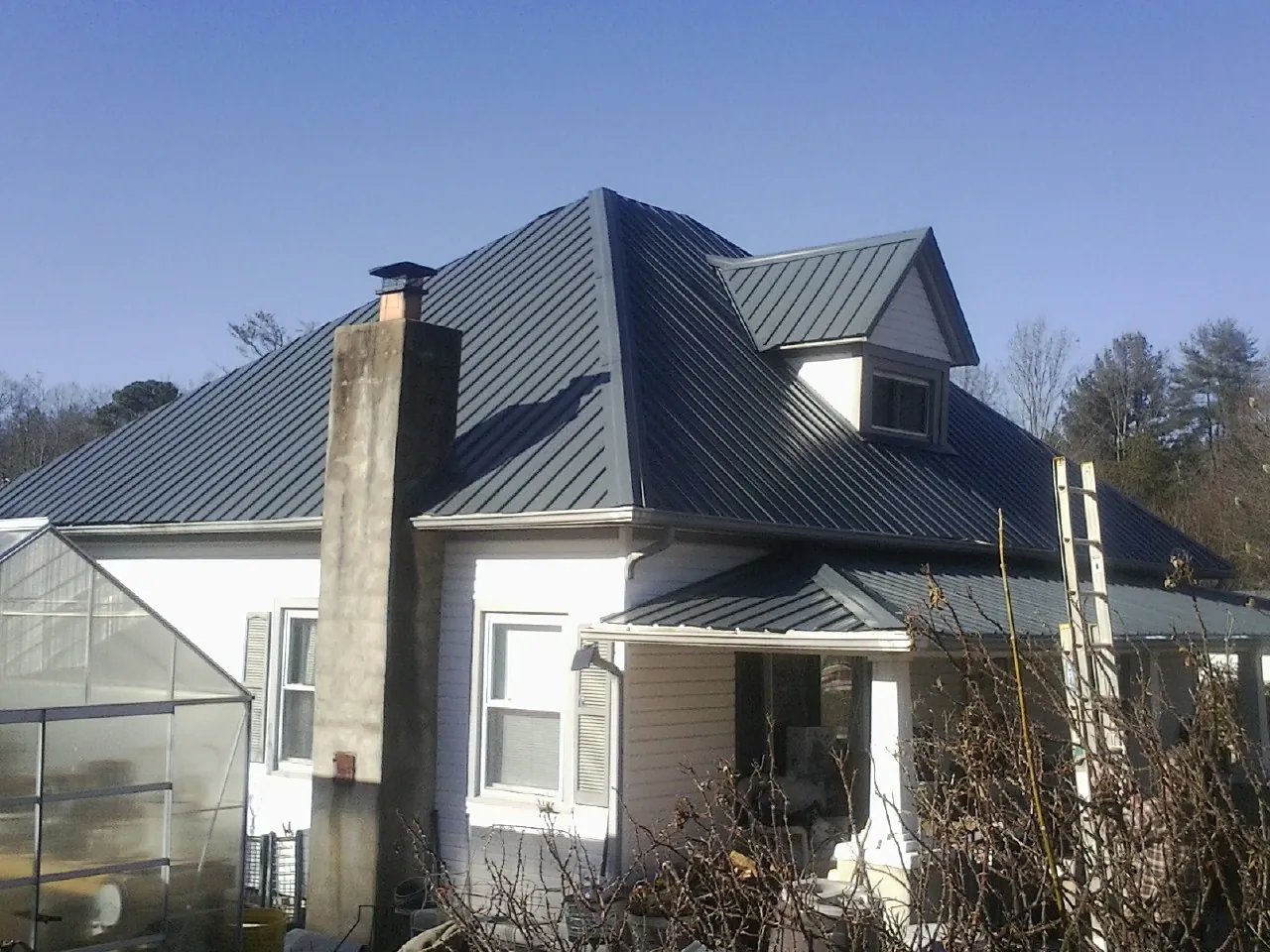 Dark blue standing seam metal roof on a white farmhouse with dormer — Slate & Tile Roof Repair by Roofing Brothers in Brenham