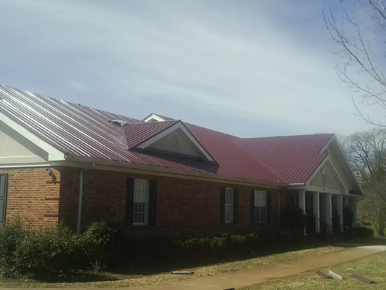 Red metal roof with gabled entries on a long brick building, from a Hail Damage Roof Repair job in Brenham