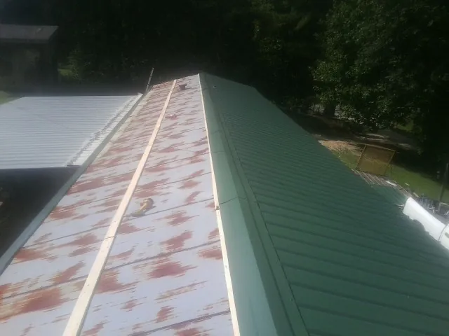 Old rusted panels beside newly installed green metal roofing — Wind Damage Roof Repair by Roofing Brothers in Brenham