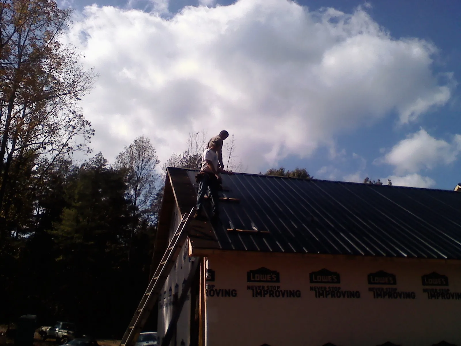 Roofer fastening dark metal panels high against a cloudy sky, from a Roof Inspection job in Brenham
