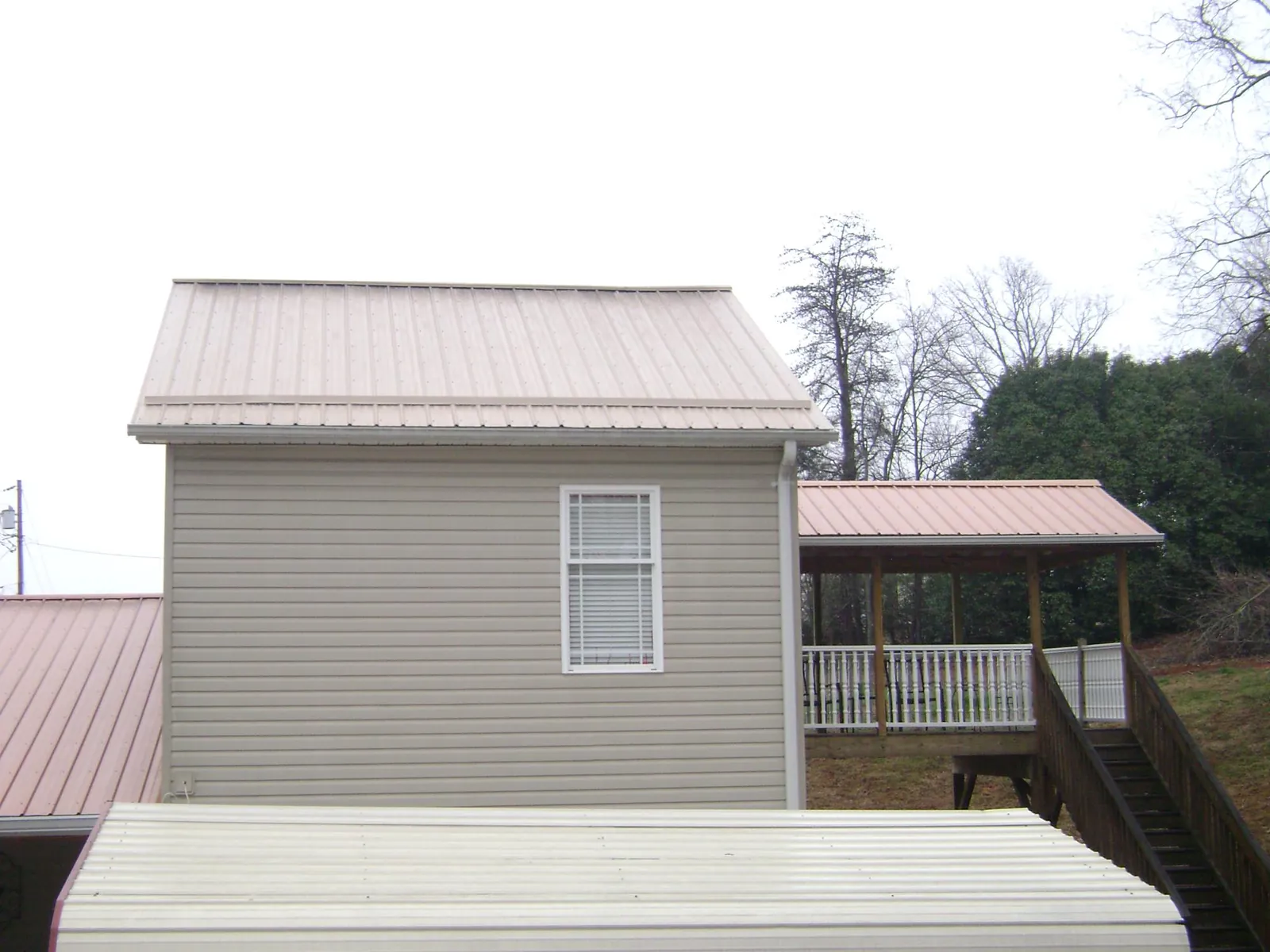 Tan metal roofs on a two story addition and attached porch, from a Roof Replacement job in Brenham