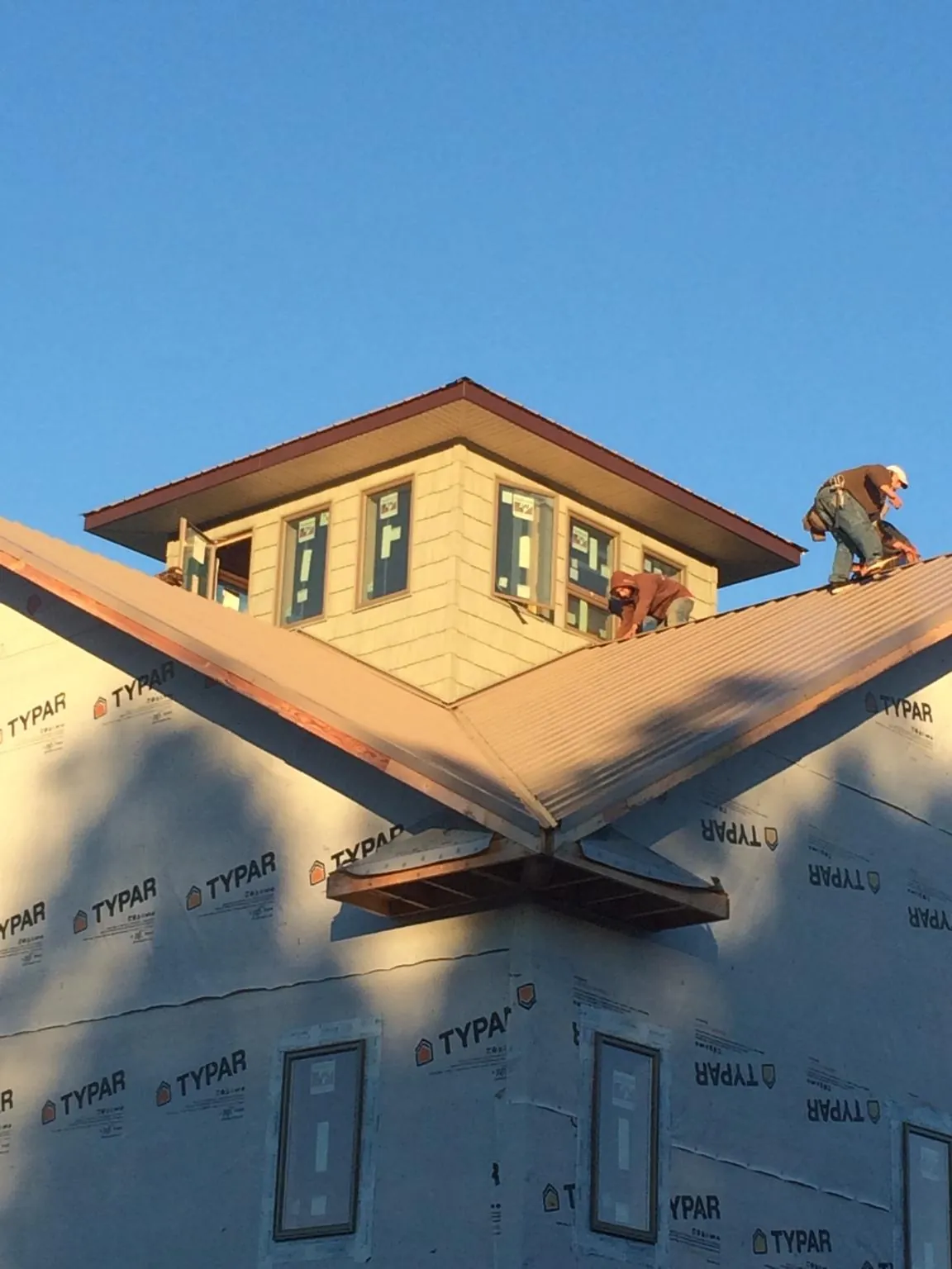 Roofers working around a rooftop cupola on a new metal roof at sunset — Roof Waterproofing in Brenham by Roofing Brothers